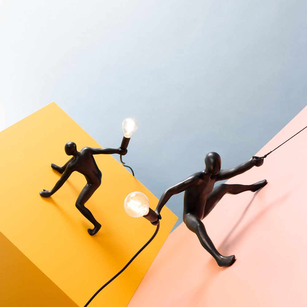 Two black figurines holding light bulbs on a colorful background