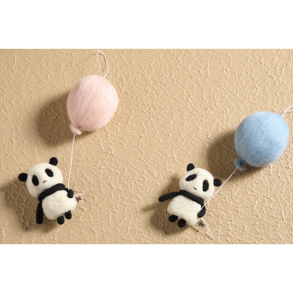 Two panda-shaped balloons with pink and blue balloons on a beige background