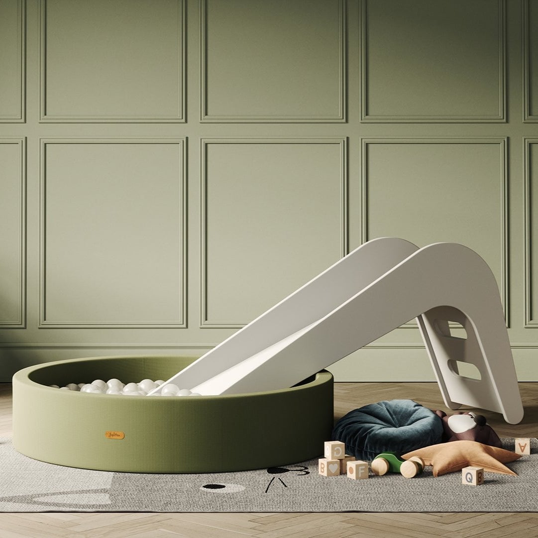 Children's play area with a slide and ball pit against a green paneled wall.