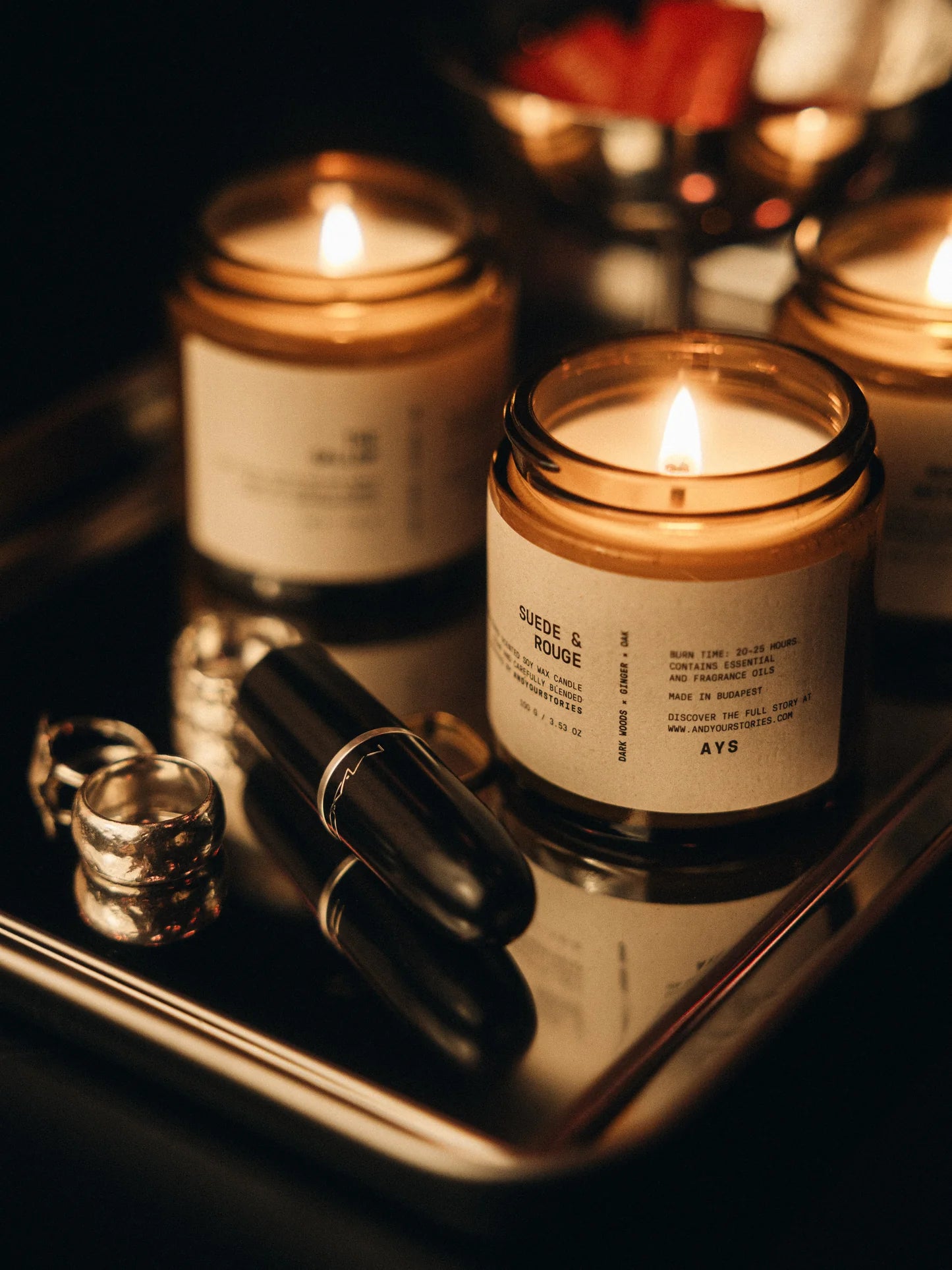 Candle with a visible brand label on a reflective surface with other candles and objects.