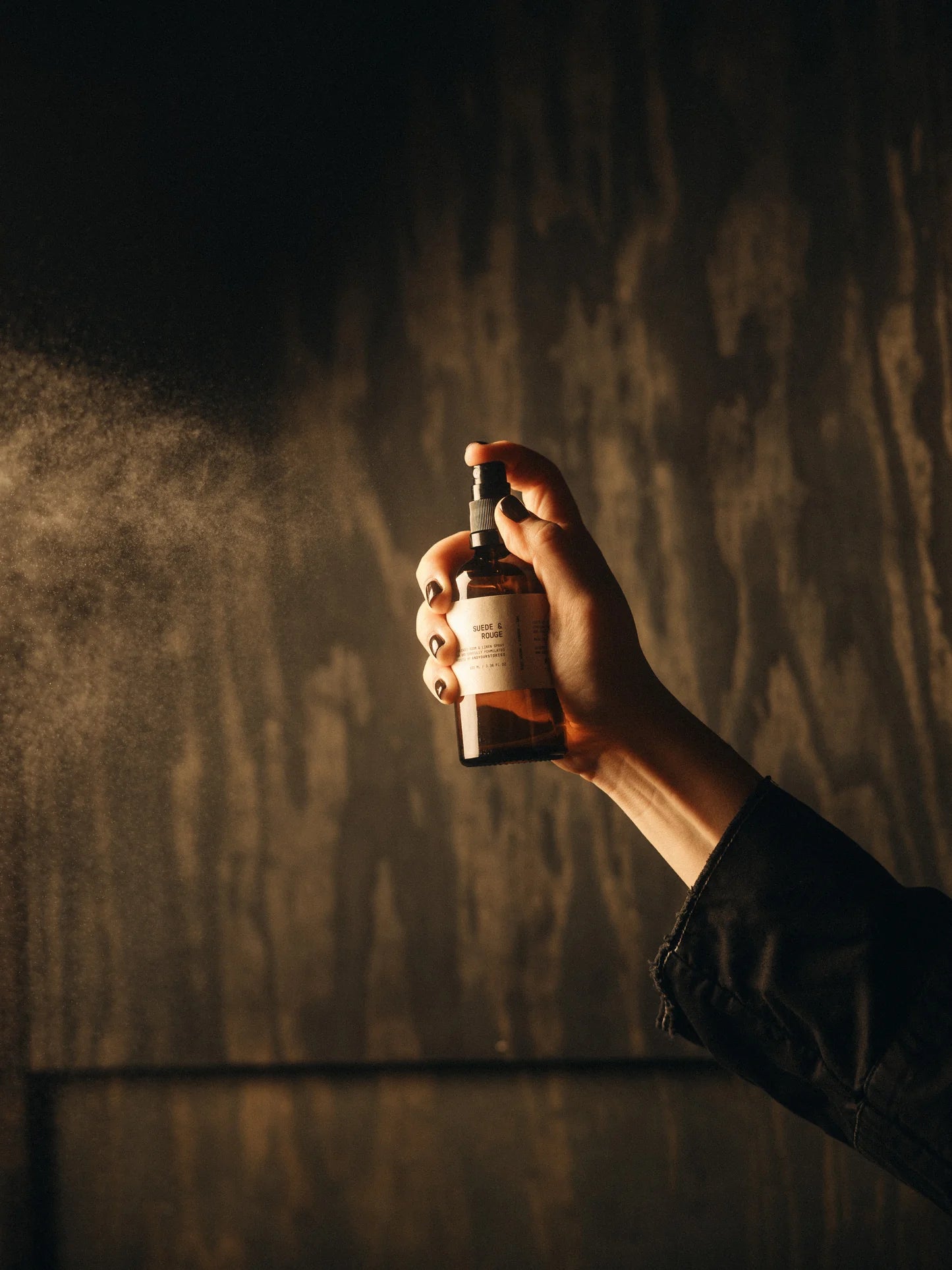 Hand holding a scented spray bottle against a dark textured wall