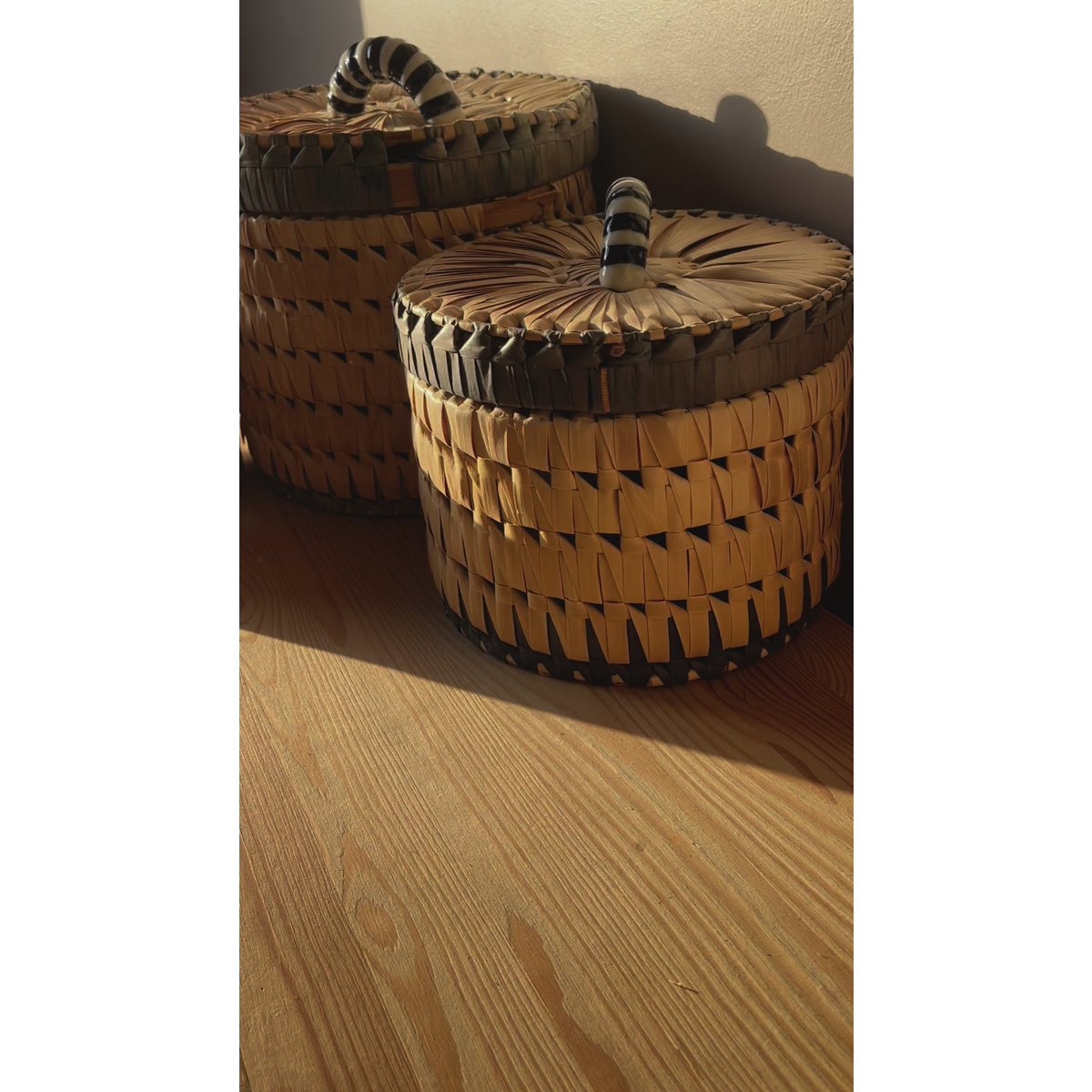 Two woven baskets with striped handles on a wooden surface