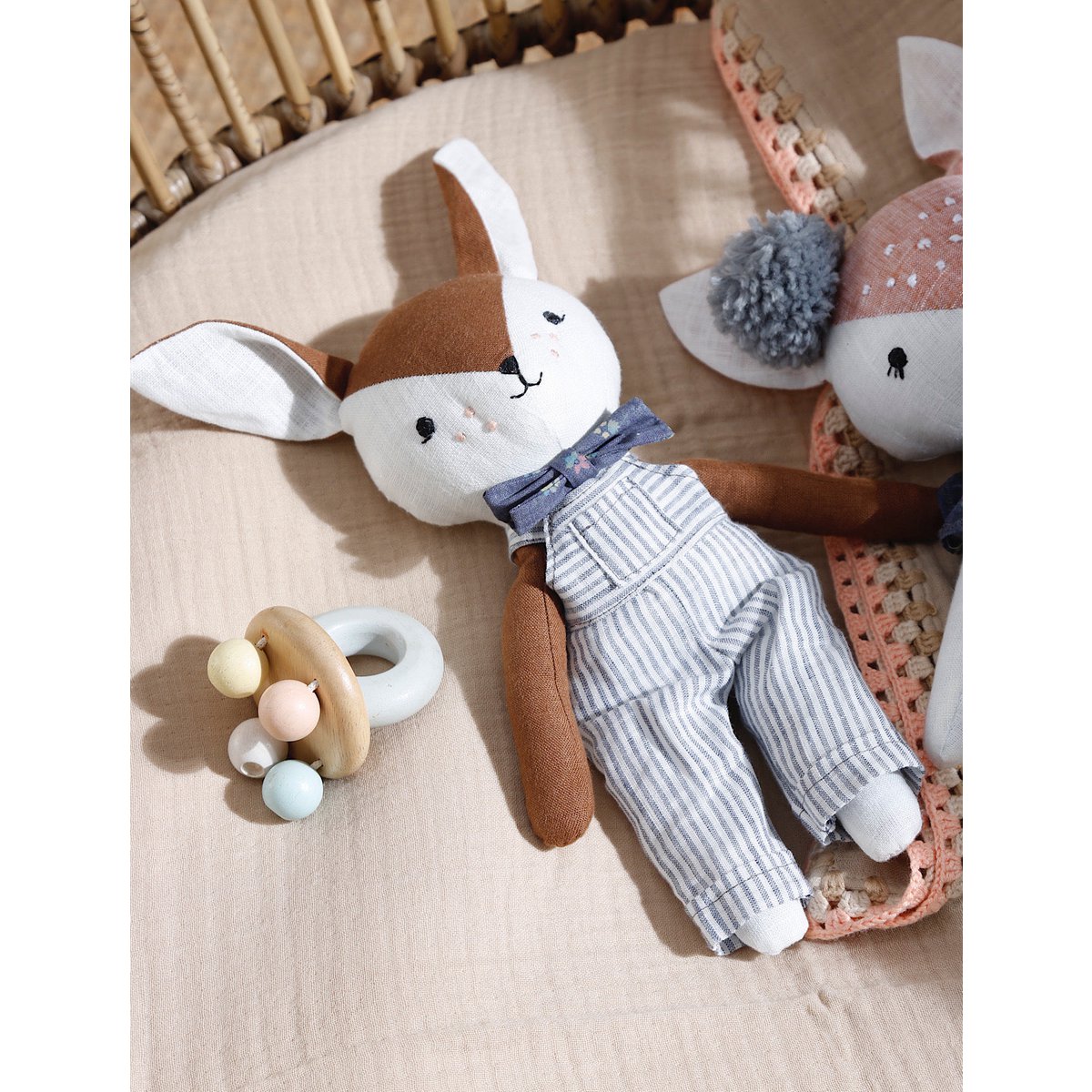 Plush toy rabbit with a bow tie and baby rattle on a textured surface
