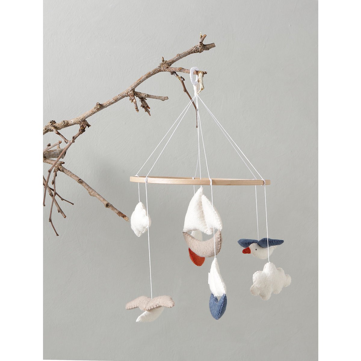 Decorative mobile with birds and clouds hanging from a branch on a gray background