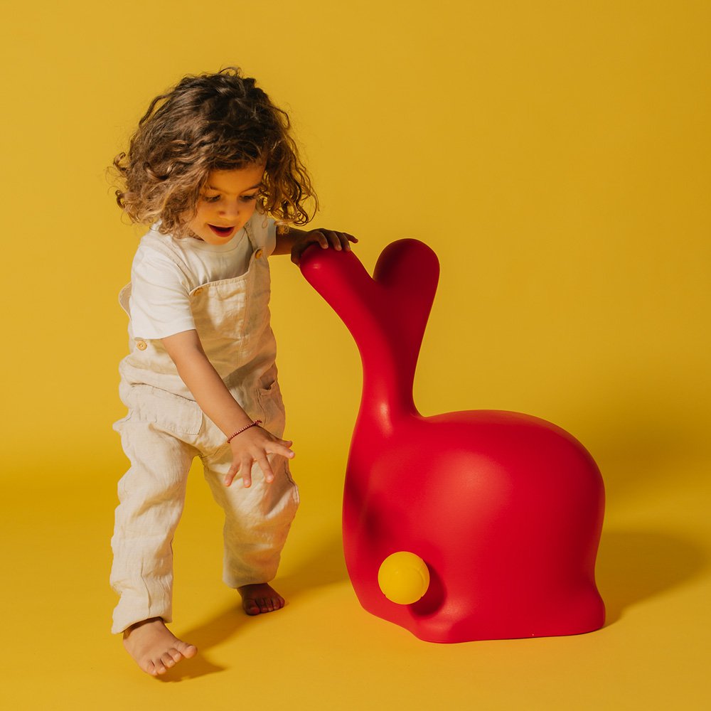 Child playing with a red rabbit-shaped chair against a yellow background