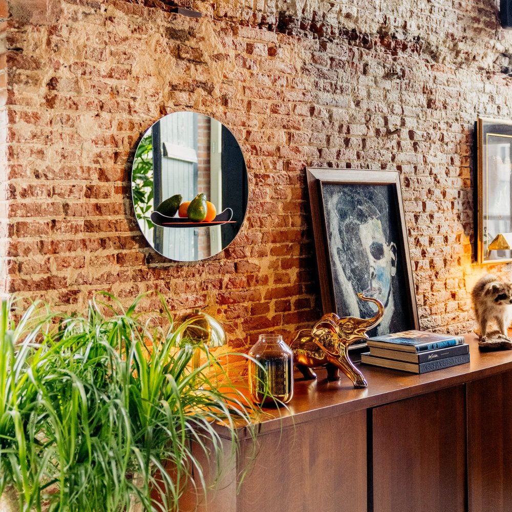 Brick wall with a round mirror, books, and decorative items on a wooden surface.