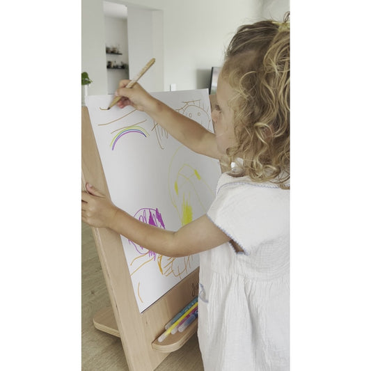 Child drawing on a white board with colorful crayons in a minimalistic room.