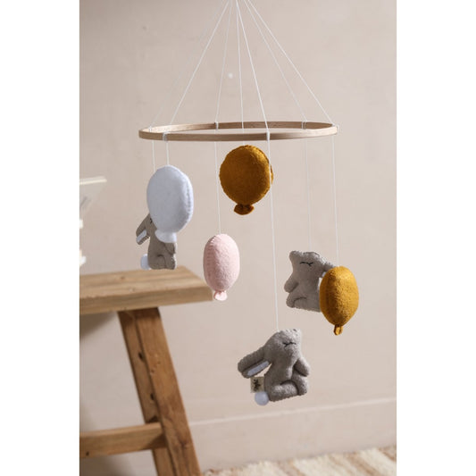 Children's mobile with hanging toys and balls on a wooden stand against a light wall.