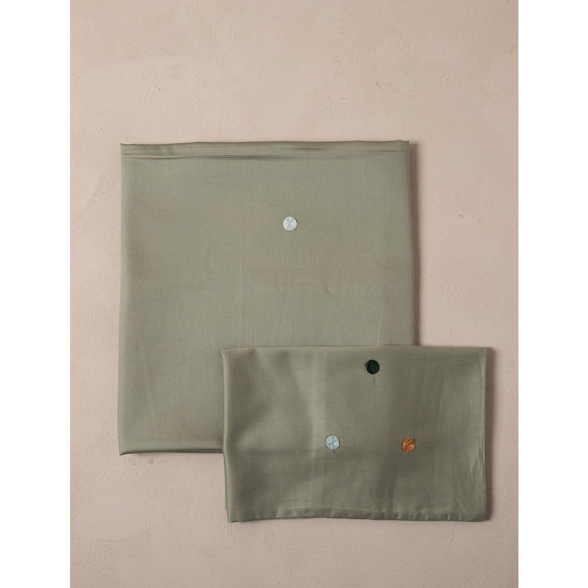 Two green fabric pouches with colorful buttons on a beige background