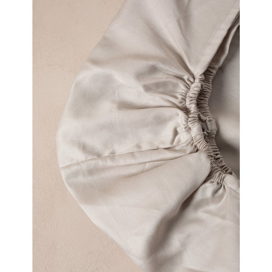 Close-up of a beige fitted sheet with elastic waistband on a neutral background