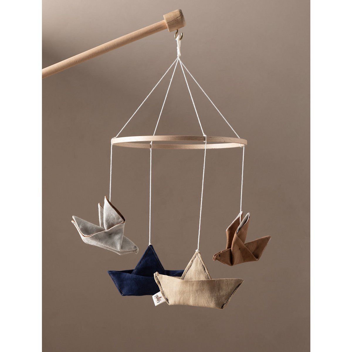 Hanging mobile with paper boat and bird designs on a plain background