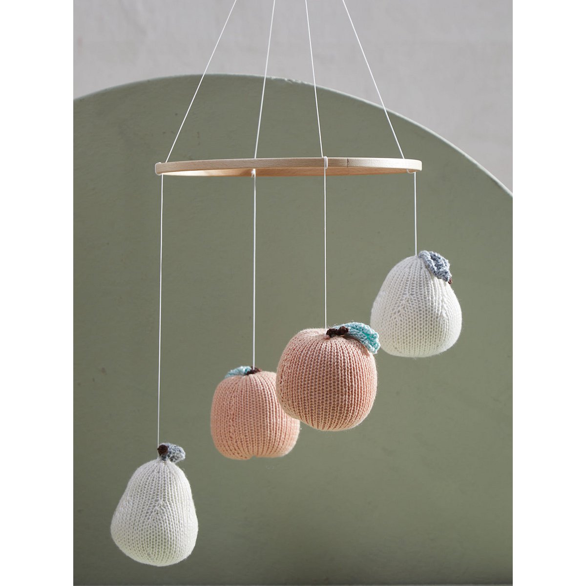 Knitted fruit-shaped mobile hanging against a plain background
