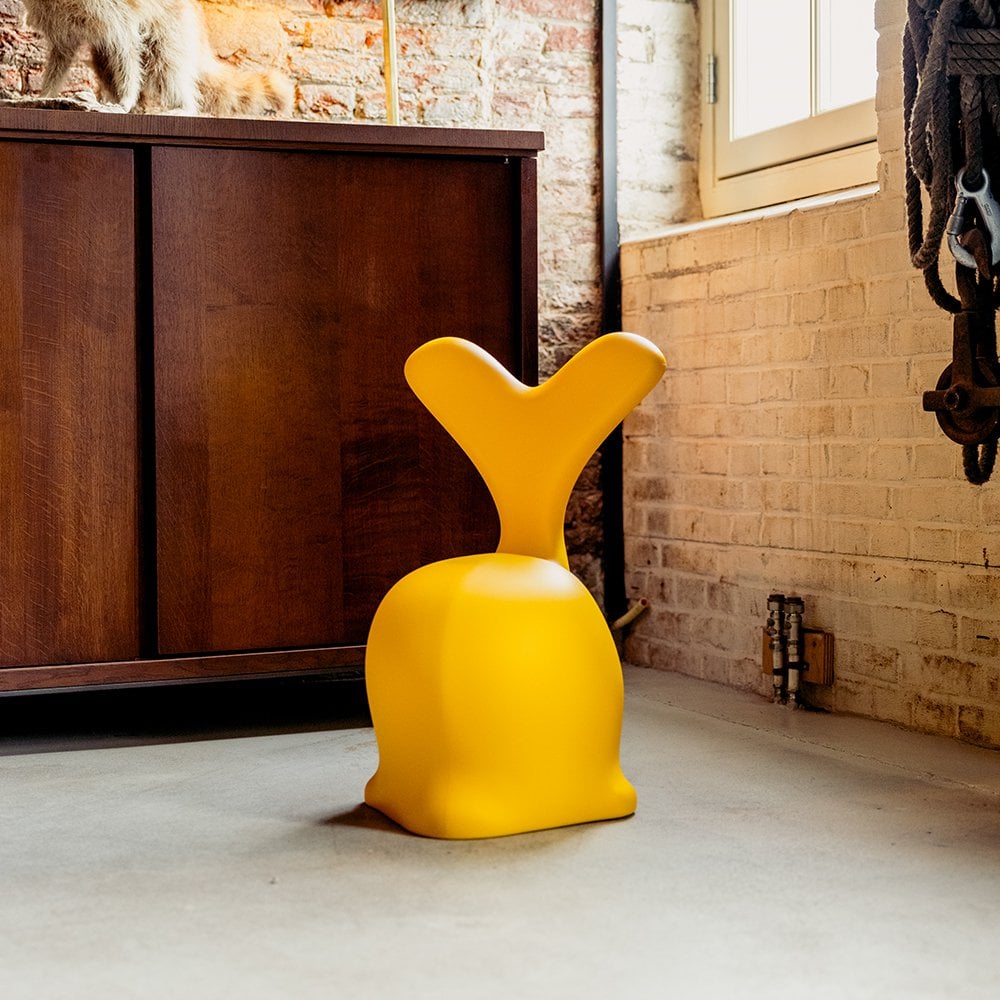 Yellow chair with a unique design in a room with brick walls and wooden furniture.