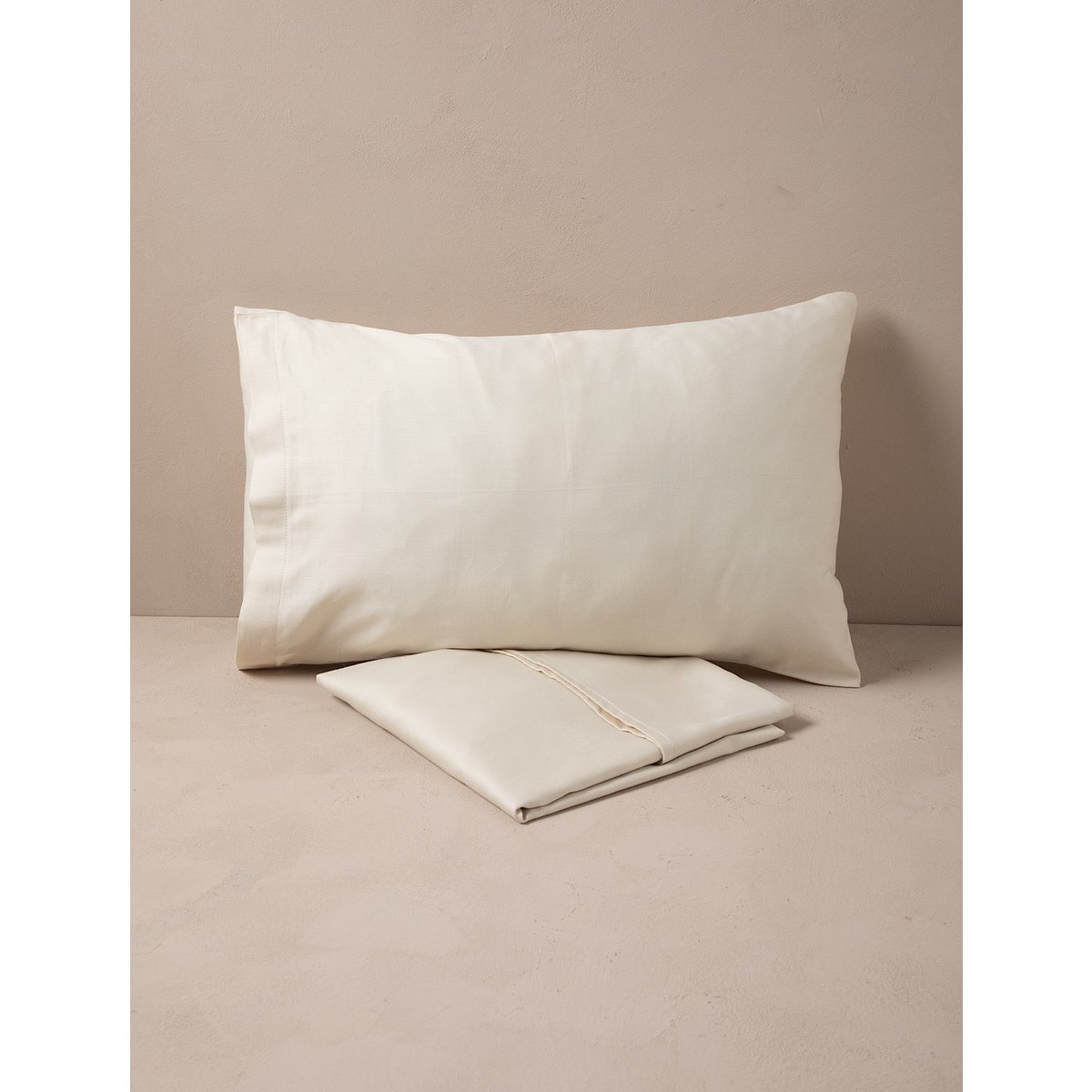 Beige pillow and folded sheet on a beige surface with a neutral background