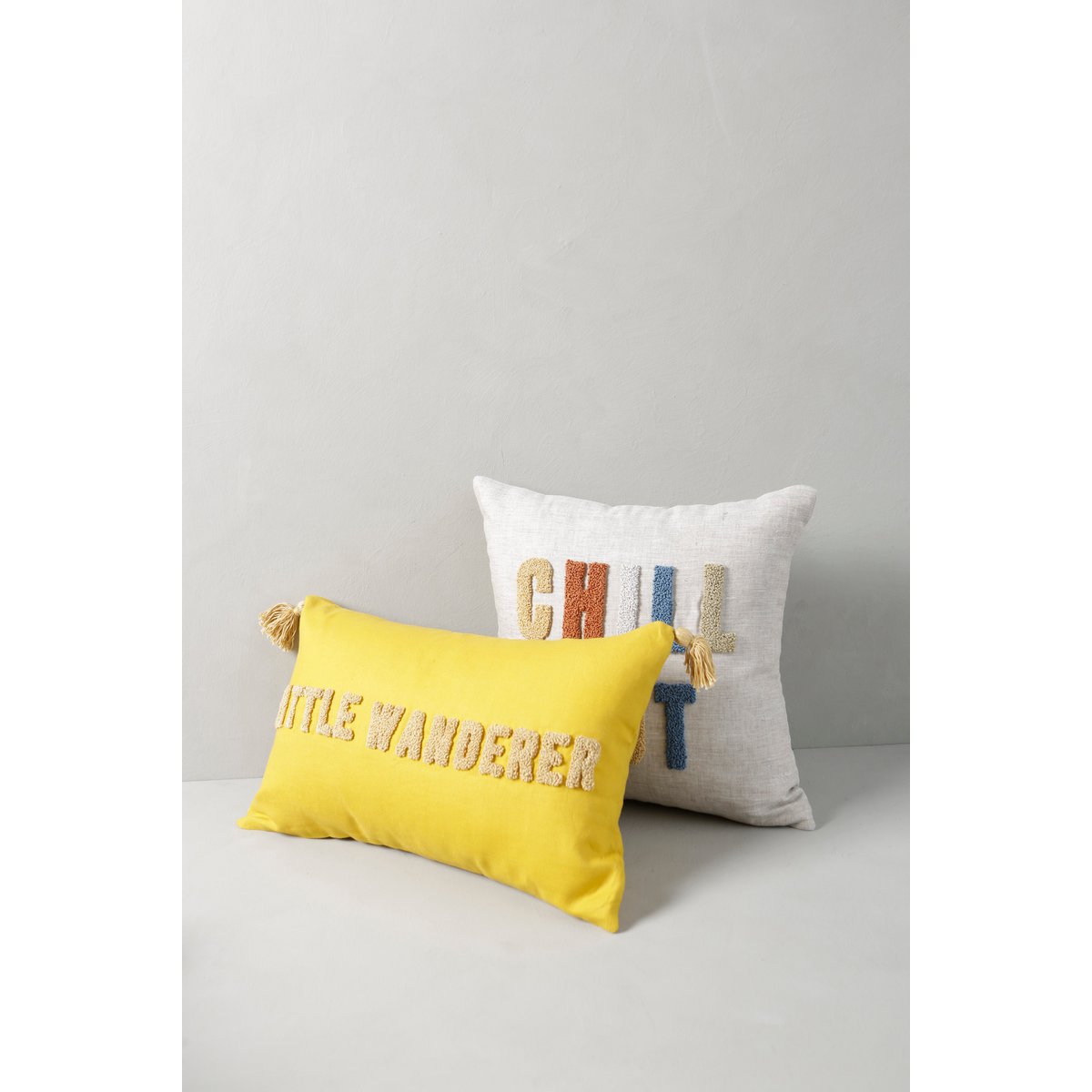 Yellow pillow with 'Little Wanderer' text and white pillow with 'Chilla' text on a light gray background