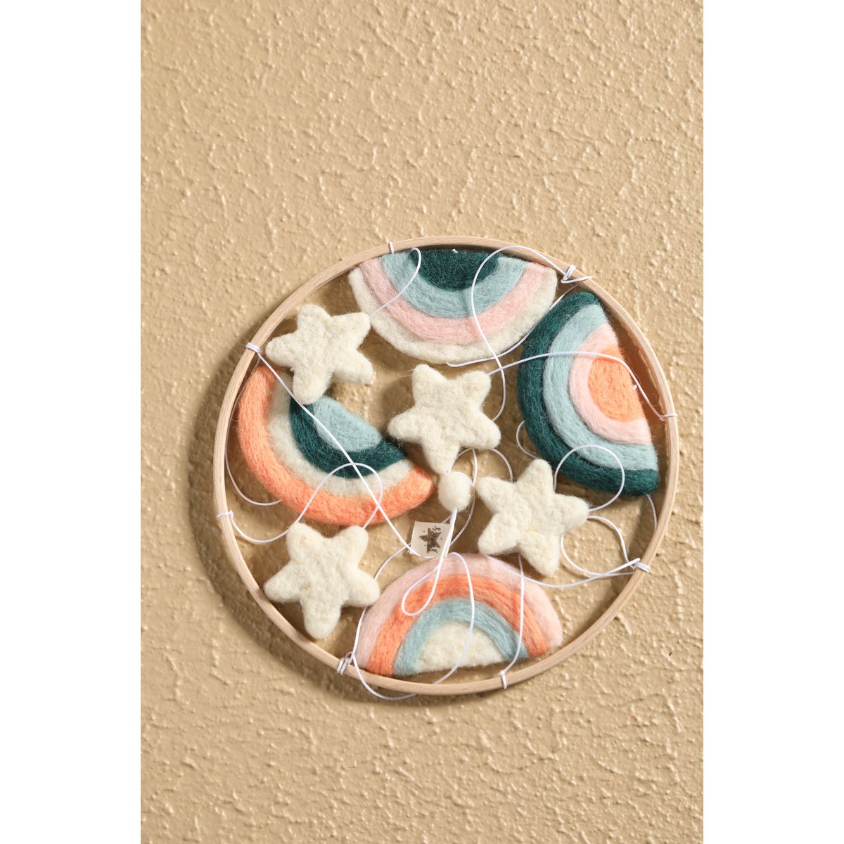 Decorative set of felt rainbow and star shapes in a wooden circle on a beige background
