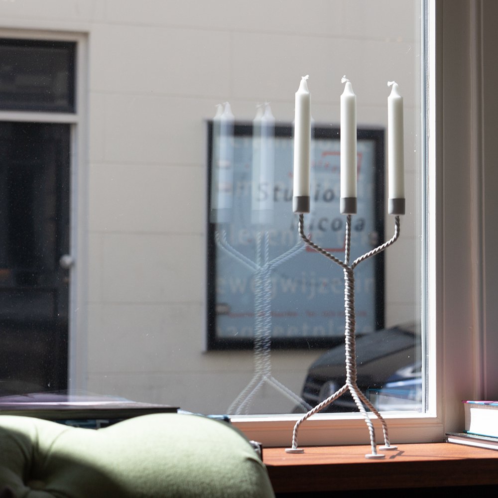 Candle holder with three candles on a windowsill, reflecting a blurred indoor setting.