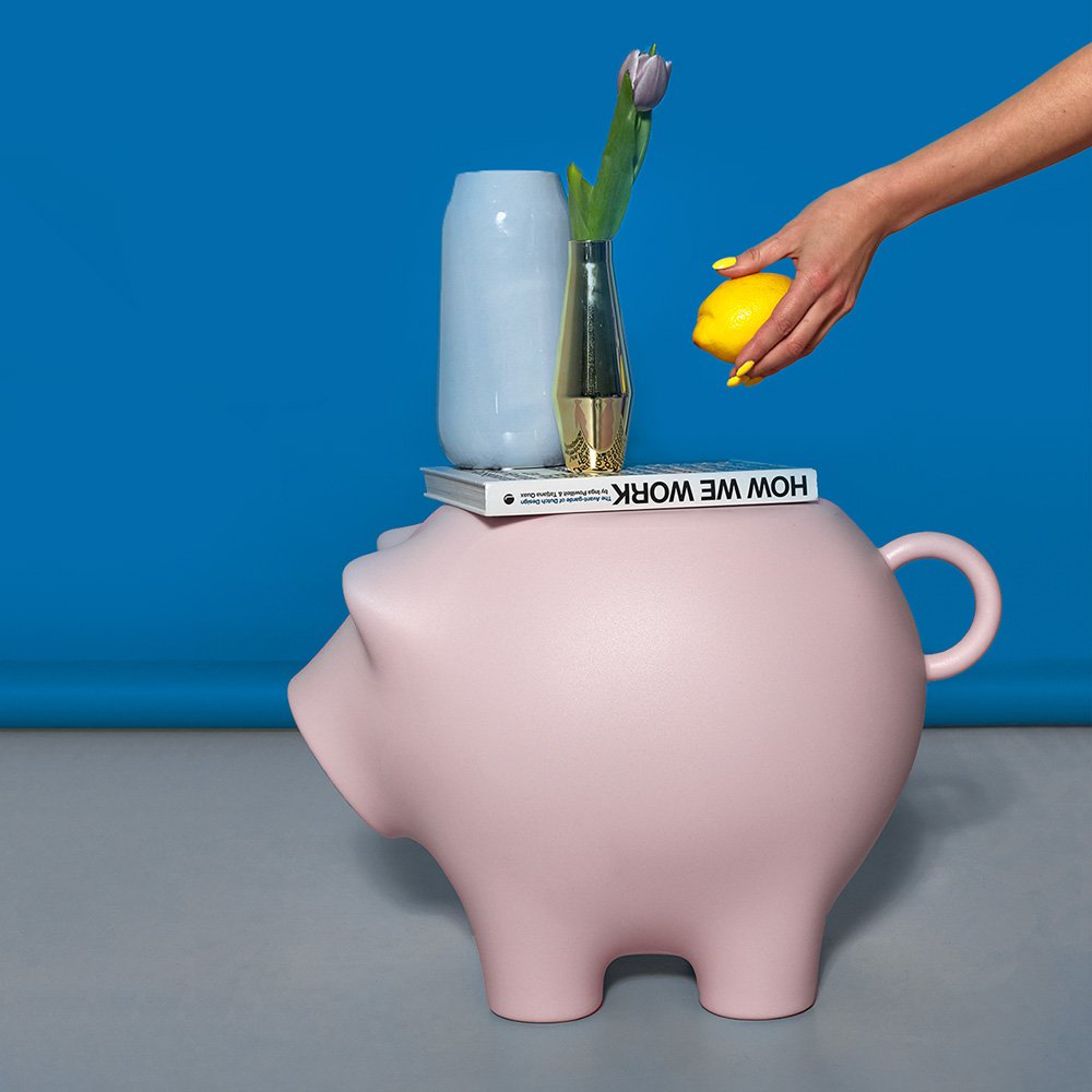 Pink piggy bank with a hand holding a lemon, blue wall, and gray surface.