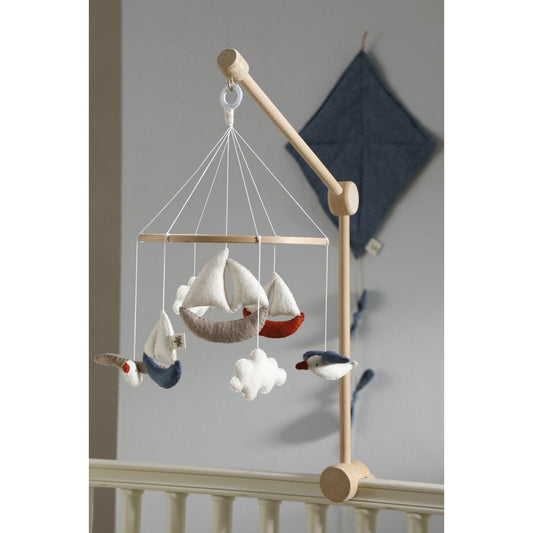 Wooden crib mobile with sailboats and birds hanging from it against a neutral background