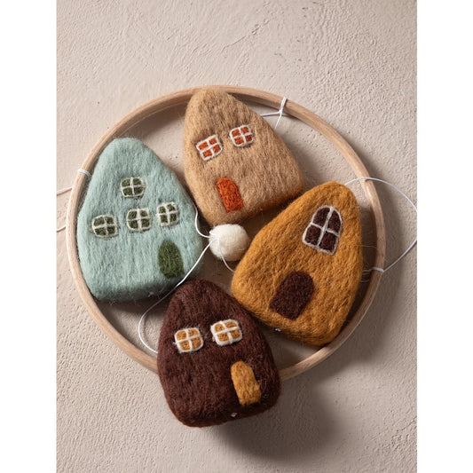 Four felted house-shaped toys on a round wooden tray against a beige background