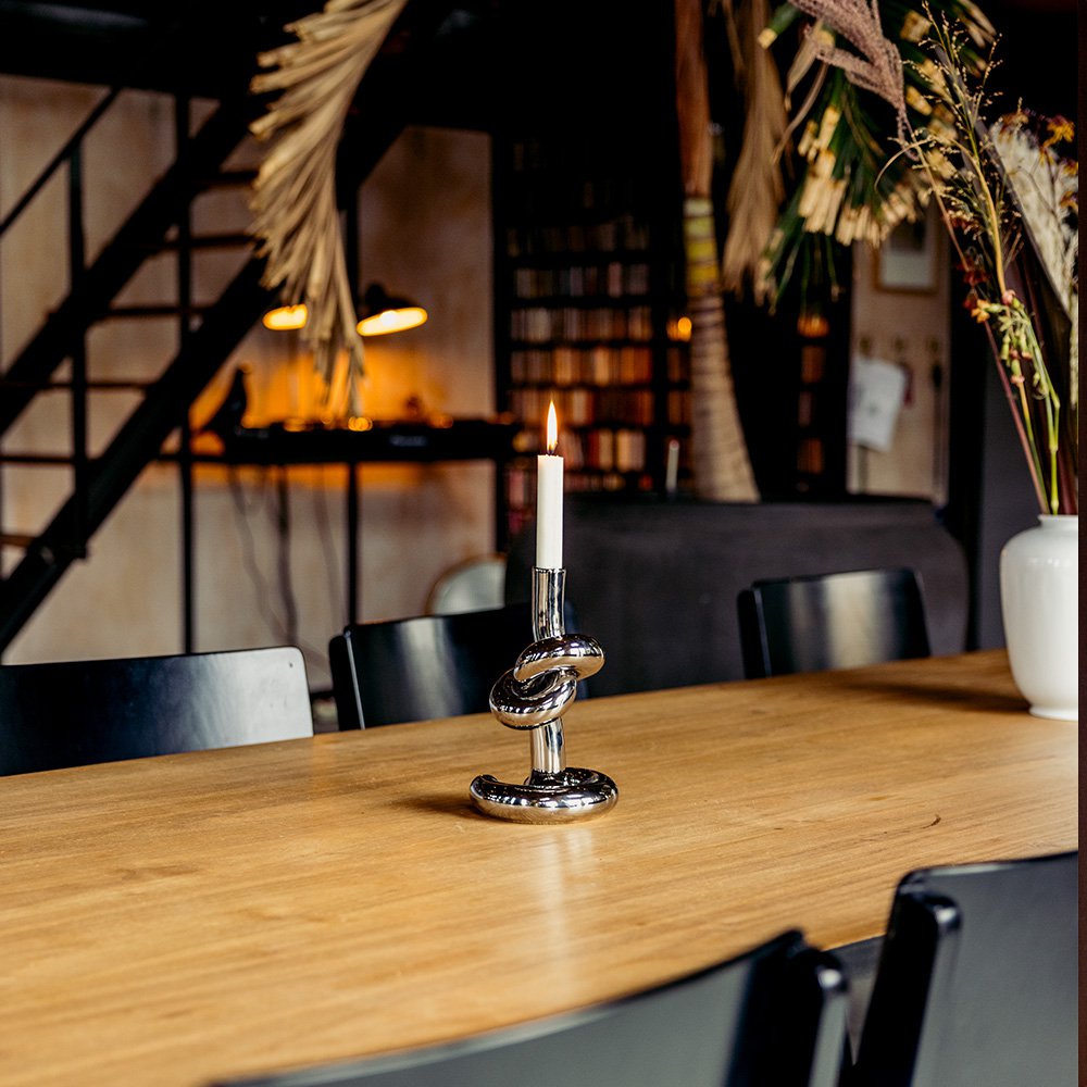 Candle in a decorative holder on a wooden table with a blurred indoor setting