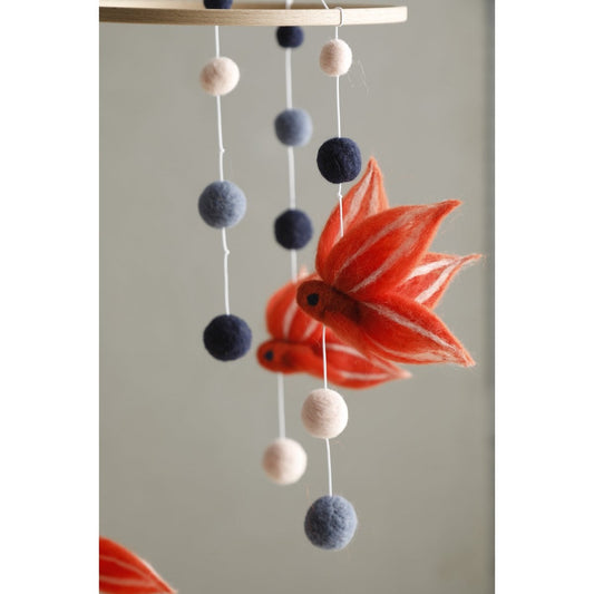 Decorative mobile with felt balls and a fish-shaped pendant on a plain background