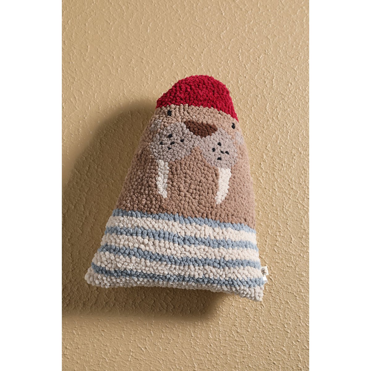 Textured knitted bell with a red top and blue and white striped base on a beige background
