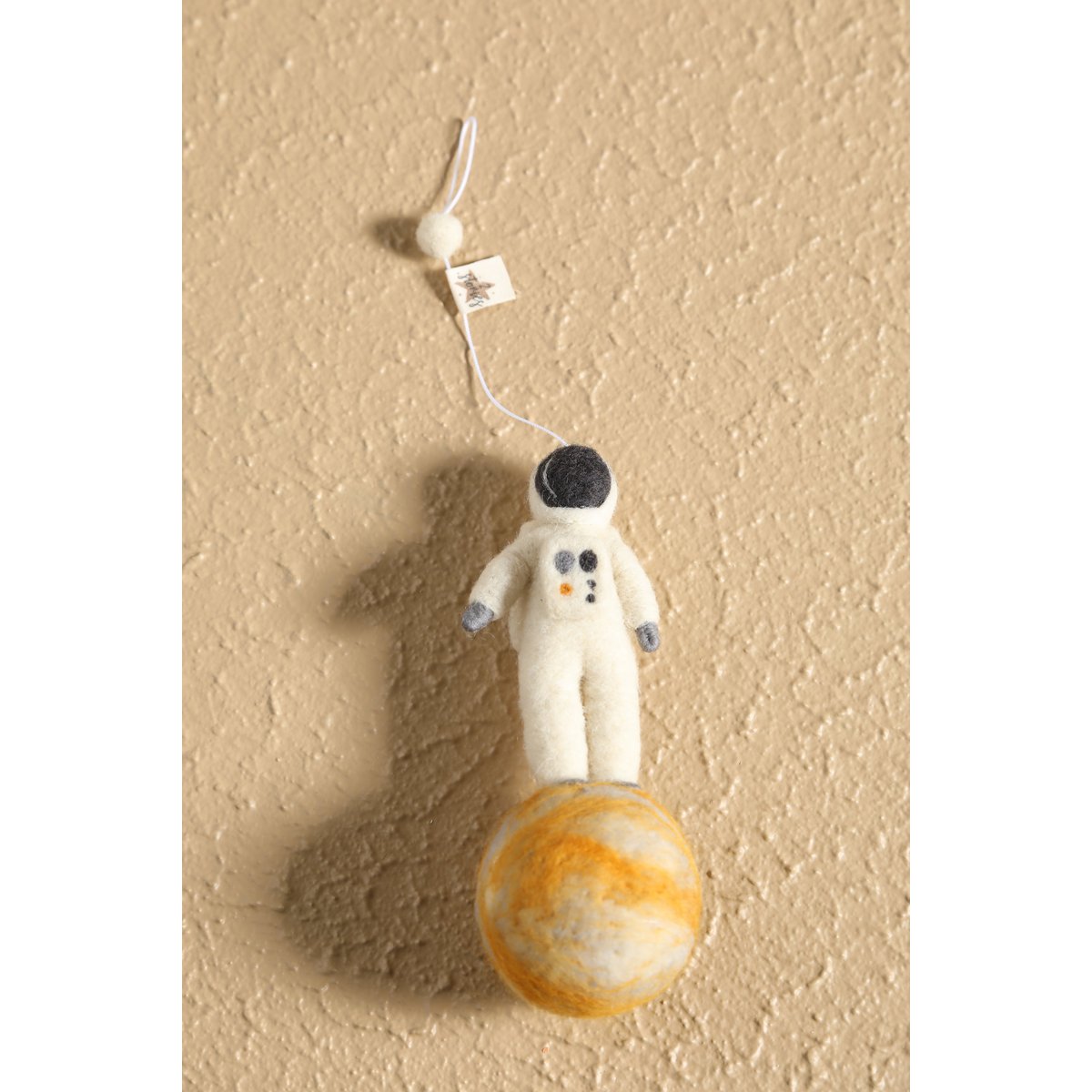 Plush astronaut toy on a small model of Jupiter against a beige background