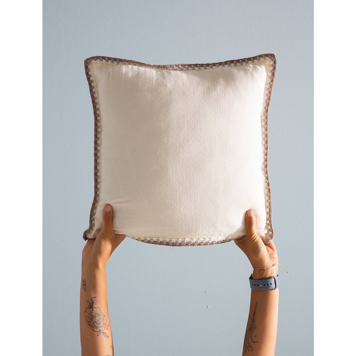 Person holding a decorative pillow with a textured border against a plain background