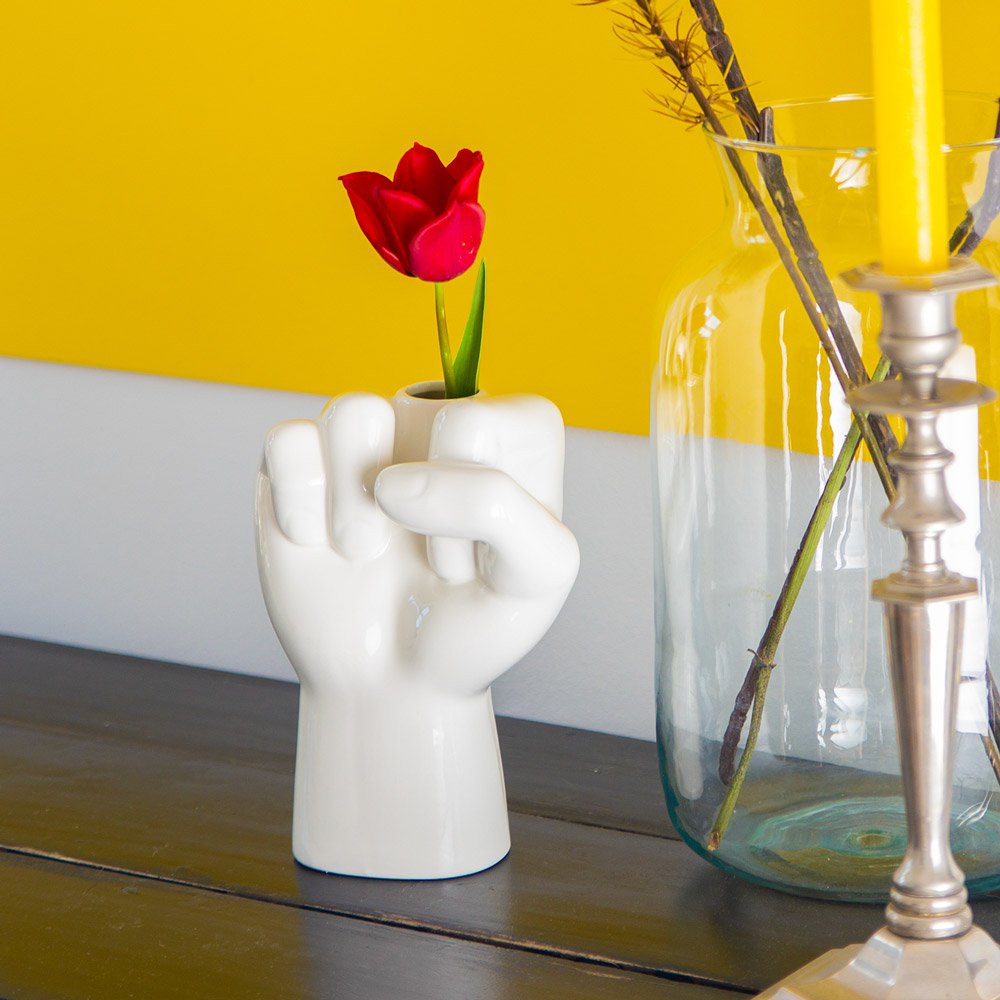 White hand-shaped vase with a red tulip against a yellow wall