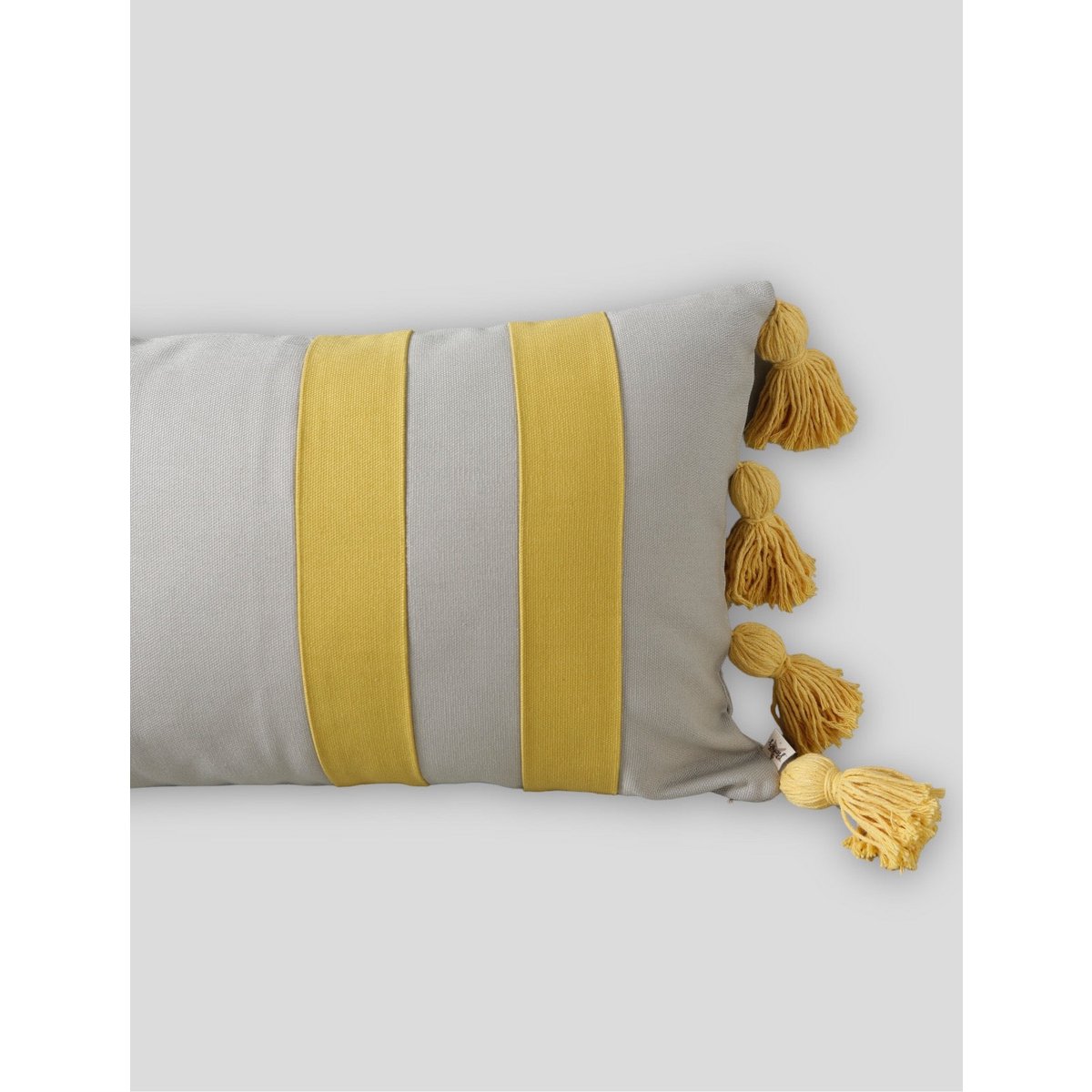 Gray pillow with mustard yellow stripes and tassels on a light gray background