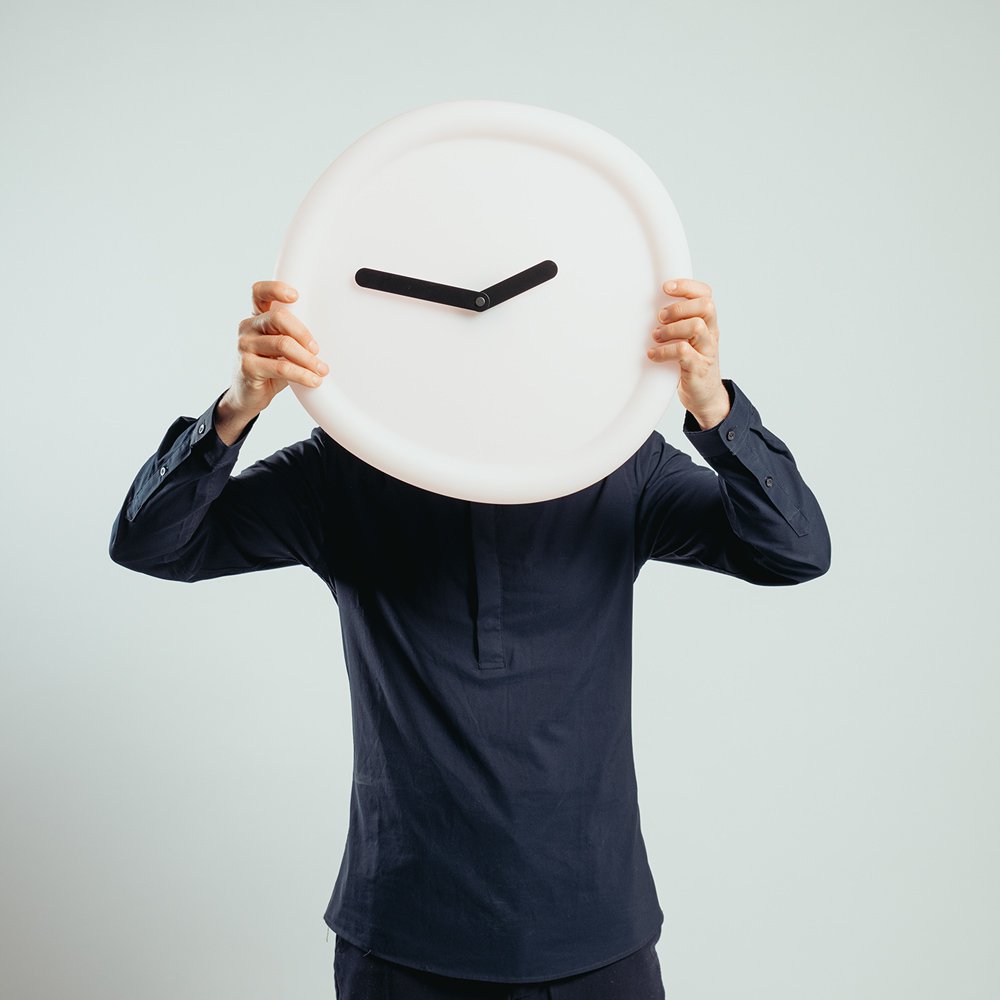 Person holding a white wall clock with black hands against a light gray background