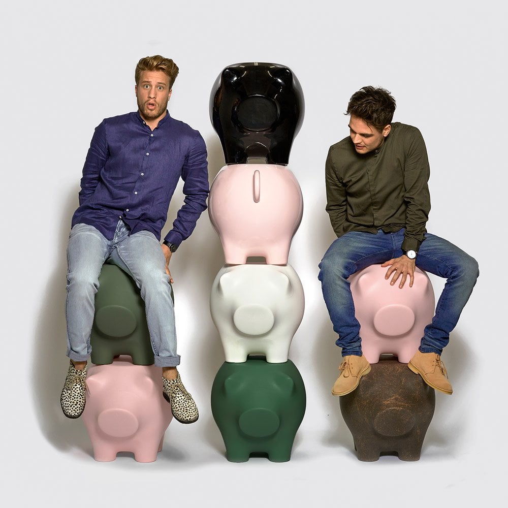 Two furniture designers sitting on colorful pig-shaped stools against a white background