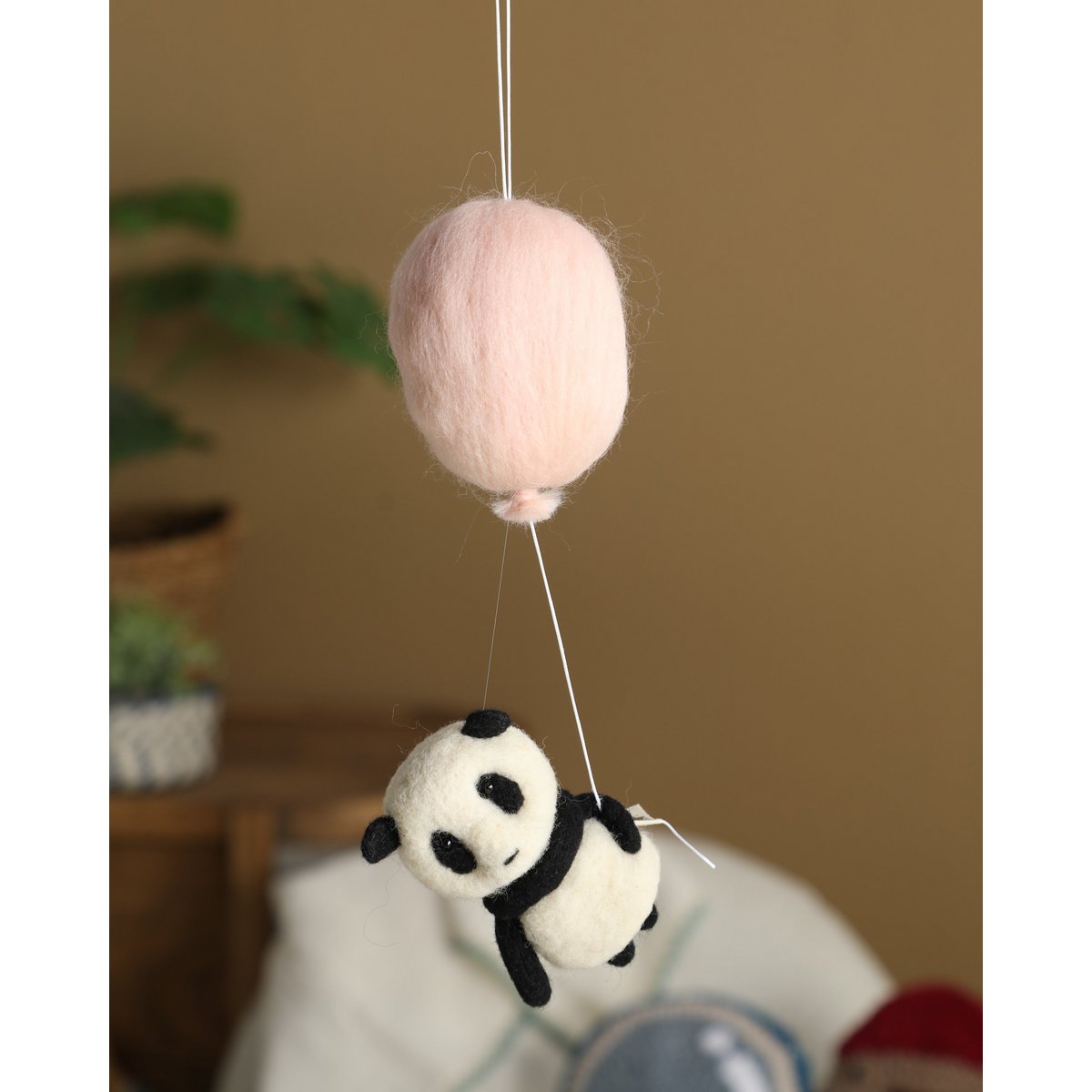 Felted panda toy hanging from a pink ball against a neutral background