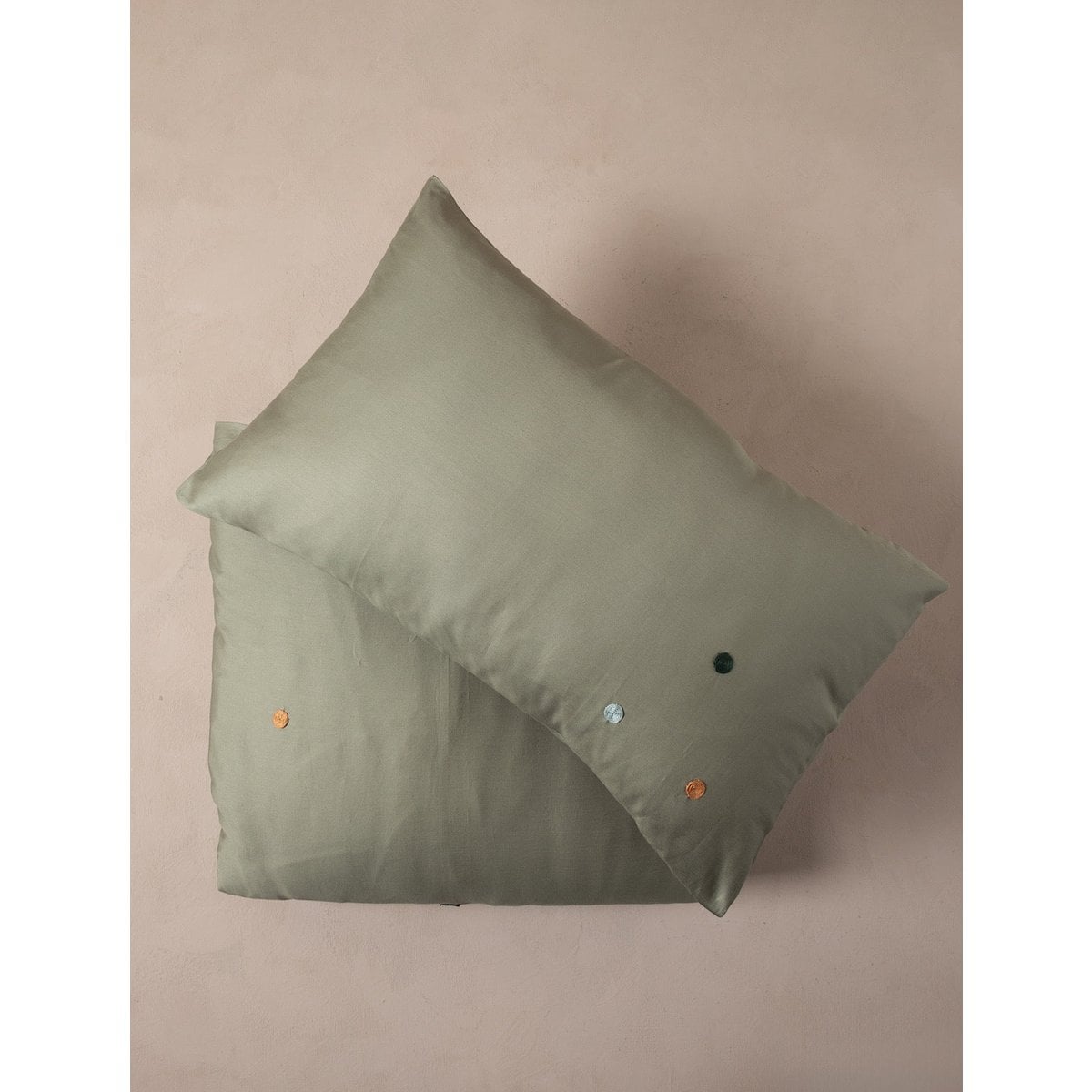 Green pillowcase with small decorative buttons on a beige background