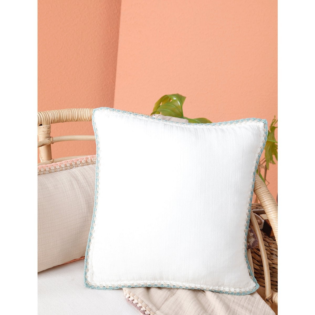White pillow with a decorative trim on a beige couch against a peach wall.