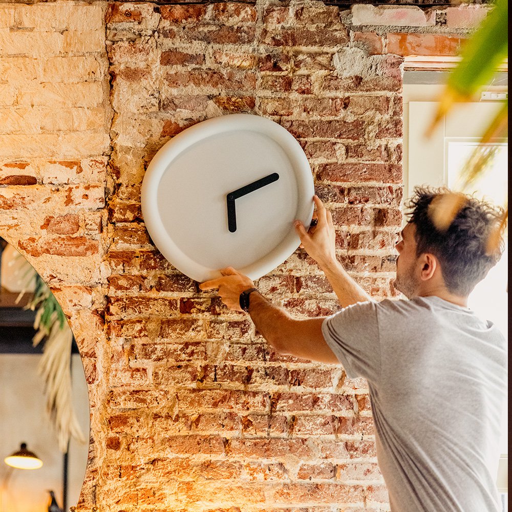 Person installing a white wall clock on a brick wall