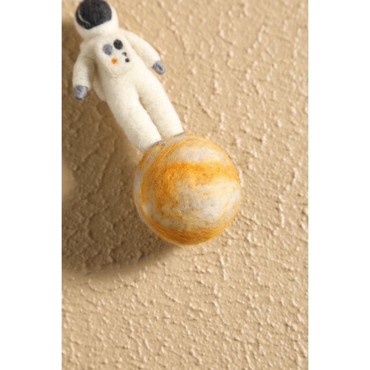 Toy astronaut holding a toy planet against a beige wall