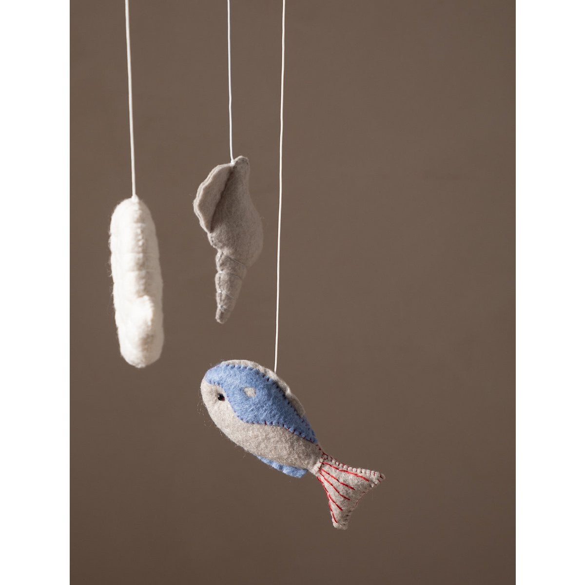 Felted fish and shell decorations hanging on strings against a brown background