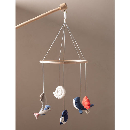 Wooden baby mobile with hanging fish and shell decorations on a beige background