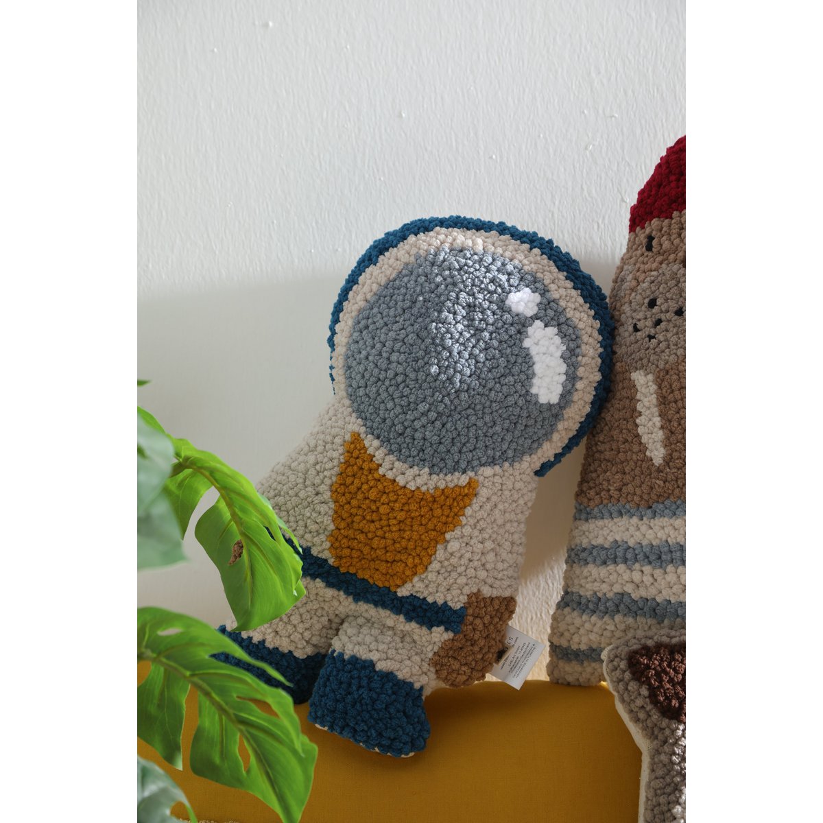 Decorative pillow shaped like an astronaut with a plant in the background