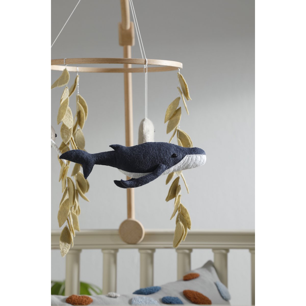 Whale-shaped toy hanging from a wooden mobile with leaves against a neutral background