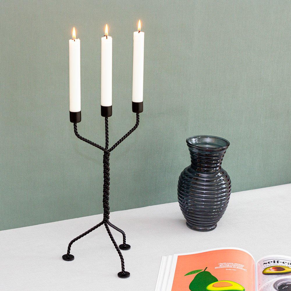 Werkwaardig Candle holder with three lit candles on a table next to a vase and magazine.