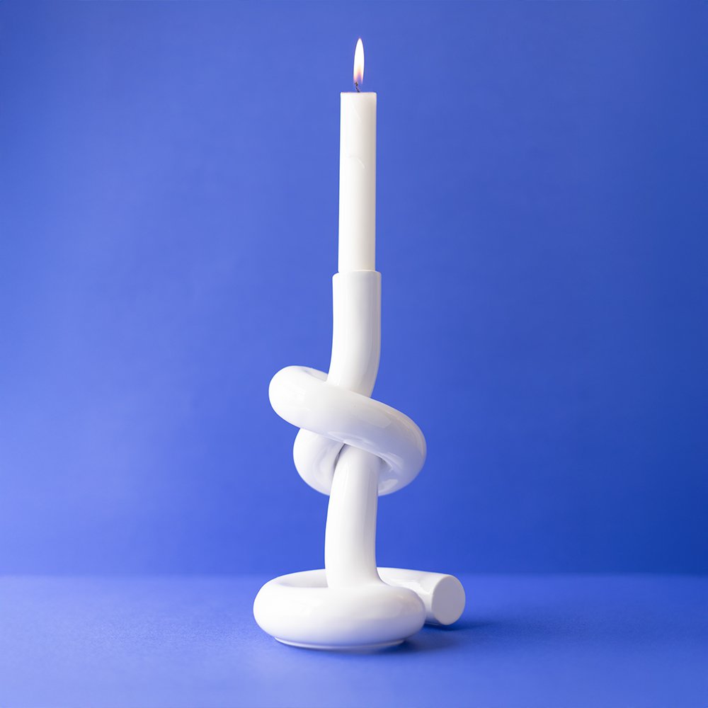 White knot-shaped candle holder with a lit white candle on a blue background