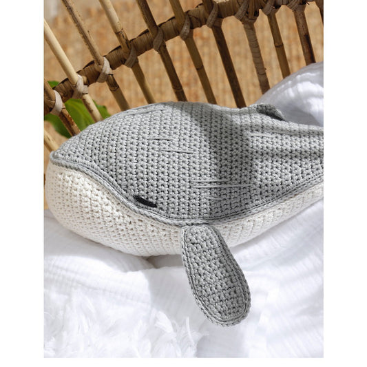 Gray crochet dolphin toy on a white surface with a wicker chair in the background