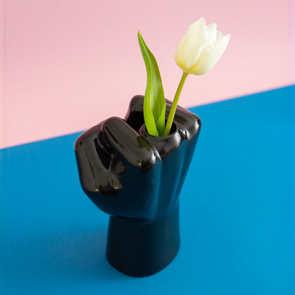 Black fist-shaped vase with a white tulip on a pink and blue background