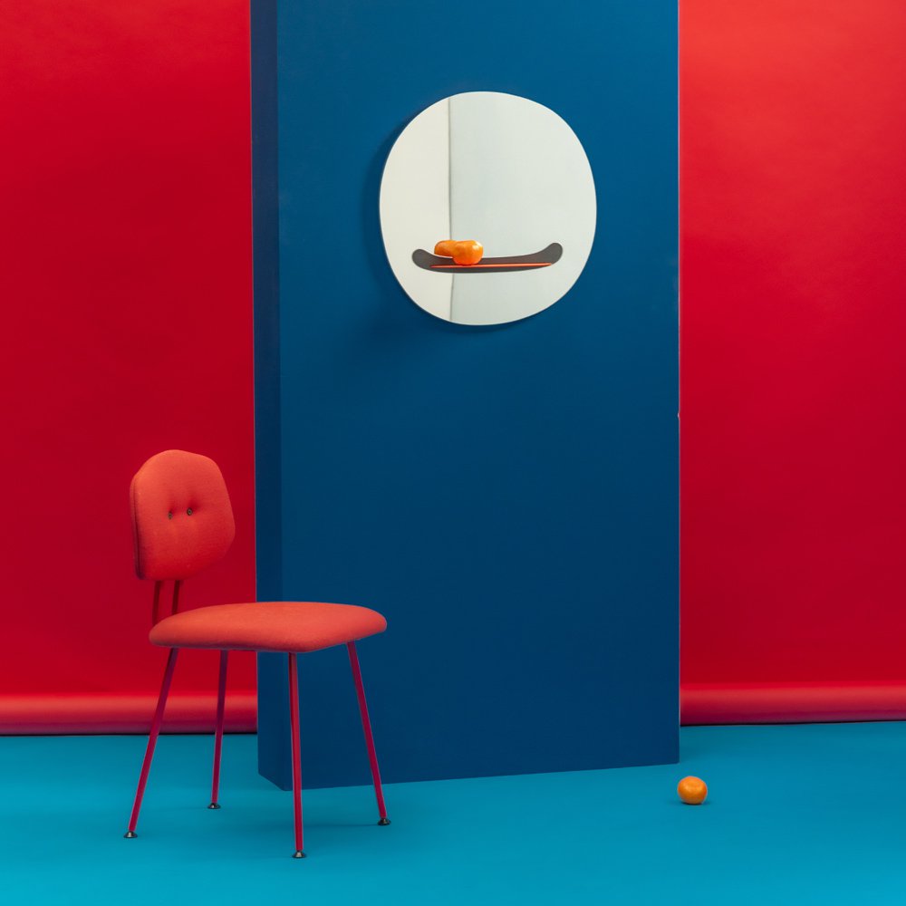 Red chair and blue wall with a round mirror featuring a skateboard design.