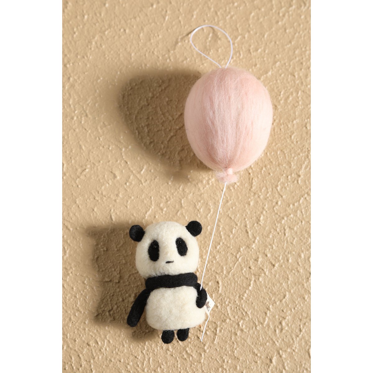 Plush panda toy with a pink balloon on a beige background