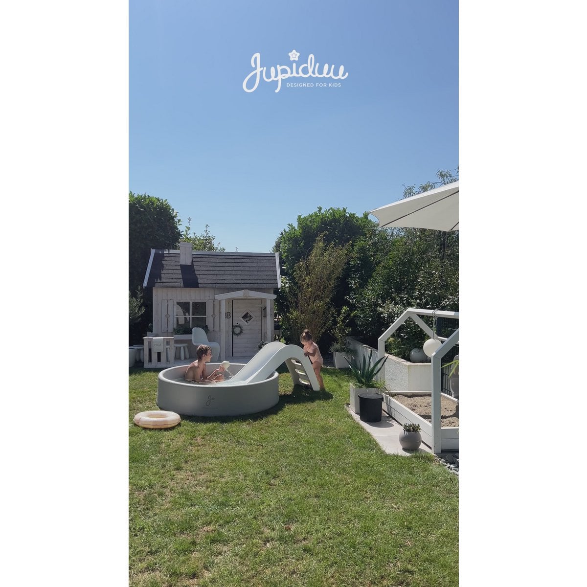 Children playing in a backyard with a slide and a pool, featuring the Jupidou brand.