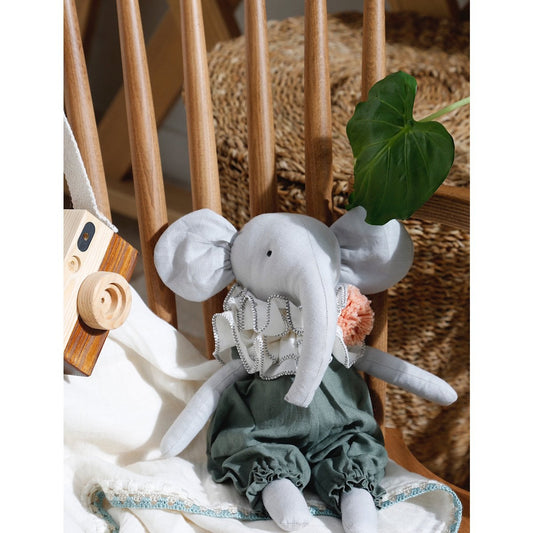 Stuffed elephant toy with a green dress sitting on a wooden chair.
